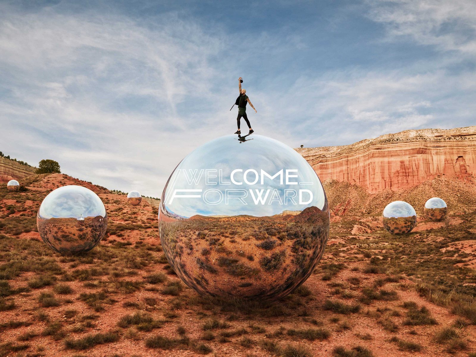 Welcome Forward campaign: an athlete on a mirrored sphere in the desert